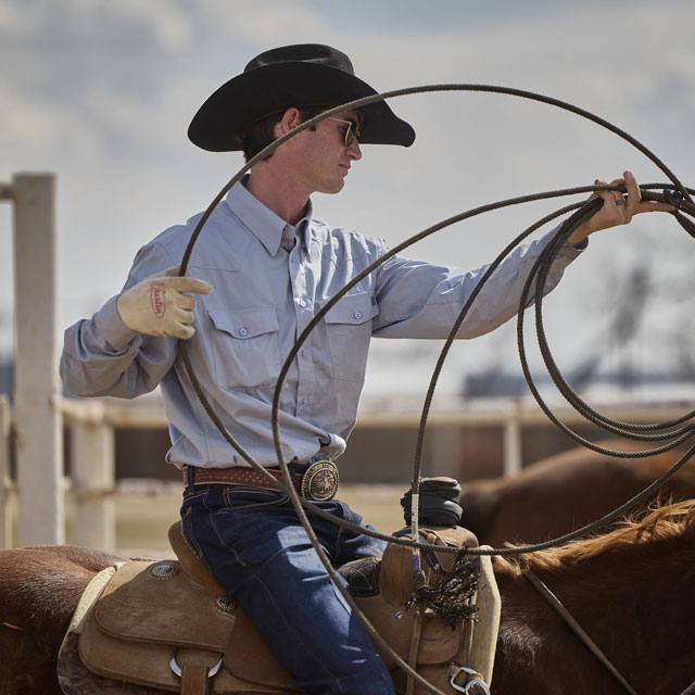 A cowboy holding a lasso while wearing a black cowboy hat.